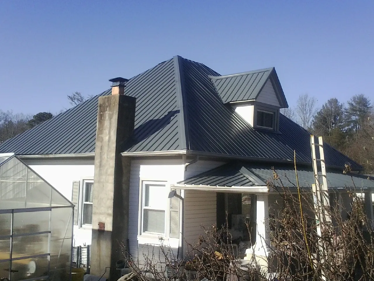 Dark blue standing seam metal roof on a white farmhouse with dormer — Slate & Tile Roof Repair by Roofing Brothers in Comstock Park