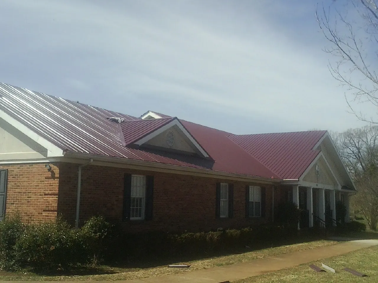 Red metal roof with gabled entries on a long brick building, from a Hail Damage Roof Repair job in Comstock Park