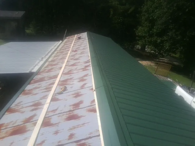 Old rusted panels beside newly installed green metal roofing — Wind Damage Roof Repair by Roofing Brothers in Comstock Park