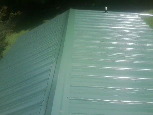 New green metal panels meeting at the ridge of a roof — Flat Roof Repair work by our crew in Comstock Park