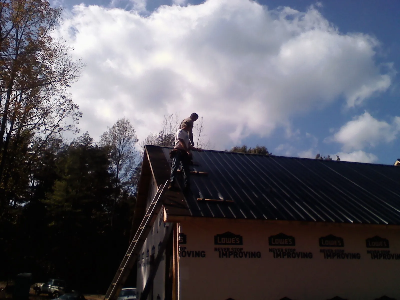 Roofer fastening dark metal panels high against a cloudy sky, from a Roof Inspection job in Comstock Park