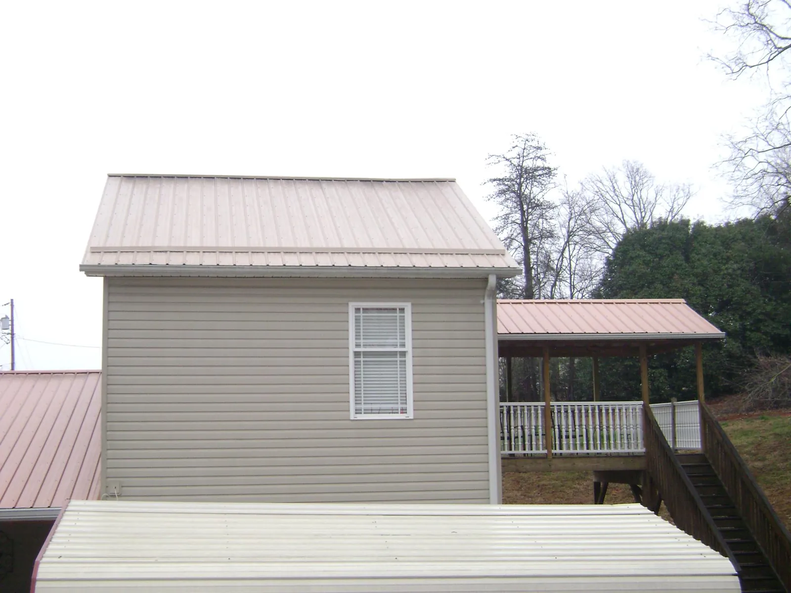 Tan metal roofs on a two story addition and attached porch, from a Roof Replacement job in Comstock Park